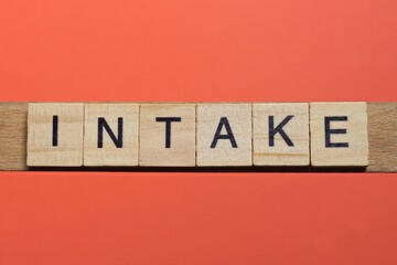 text the word intake from gray wooden small letters with black font on an red table