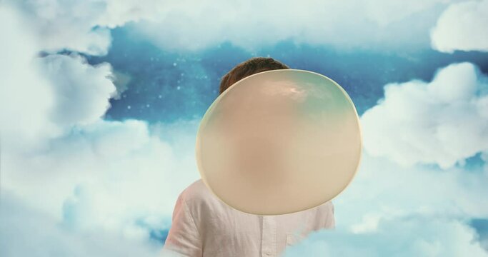 The small boy in blue skies blowing a big  bubble from bubble gum. Small boy chewing a gum and making giant bubble