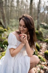 Portrait of a woman in the forest. She is sitting in a white dress on a meadow with snowdrops in a spring forest