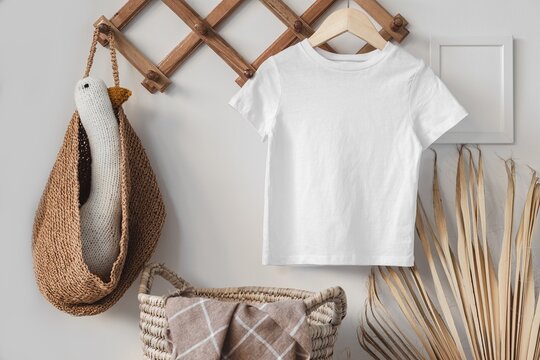 Minimalist white kid t-shirt mockup for presentation cute child sublimation designs in scandinavian boho interior with minimalistic handmade decoration and dried palm leaf