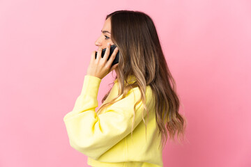Young Romanian woman isolated on pink background keeping a conversation with the mobile phone with someone