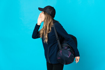 Young Romanian sport woman with sport bag isolated on blue background shouting with mouth wide open to the side