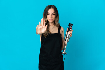 Romanian woman using hand blender isolated on blue background making stop gesture