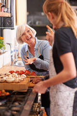 Woman, grandmother and cooking together in kitchen or teach recipe, prepare dinner or cook lunch with family. Senior mother, girl and conversation in home or talking about food or healthy vegetables