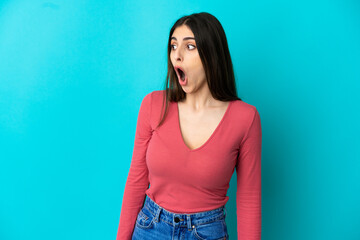 Young caucasian woman isolated on blue background doing surprise gesture while looking to the side