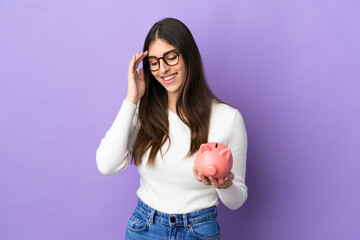 Young caucasian woman holding a piggybank isolated on purple background laughing