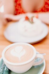 Charming woman in a restaurant, cafe on the street. She sits at the table and eats a cake with a fork. Dressed in a red sundress with white polka dots.