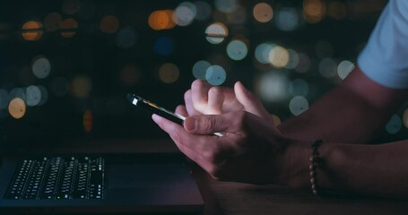 Male hand scrolling browsing on mobile phone at night time while working at laptop. Closeup person using smartphone, browsing social network. Male hand scroll through news feed on app on mobile phone - Powered by Adobe