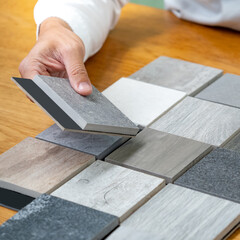 Fototapeta na wymiar Architect hand choosing sample of stone material or tile texture collection on the table in studio. Designer working for interior architecture and furniture design project.