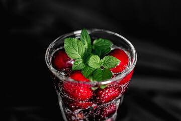 summer cocktail with cherry berries and mint sprigs in a transparent glass on a black background. bubbles in a glass. soft drink