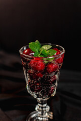 summer cocktail with cherry berries and mint sprigs in a transparent glass on a black background. bubbles in a glass. soft drink