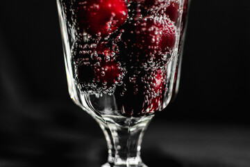summer cocktail with cherry berries and mint sprigs in a transparent glass on a black background. bubbles in a glass. soft drink