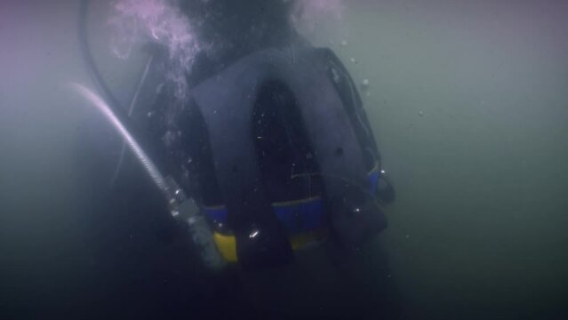 A professional diver on the seabed in the murky waters of a river estuary, close-up of the diver's helmet.