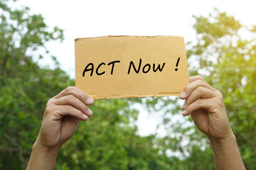 Hands hold paper sign with text  Act Now!. Concept , protest, calling for action immediately, campaign  for everyone to help limit global warming , climate change and take care of our planet.