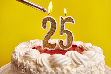 A candle in the form of the number 25, stuck in a festive cake, is lit. Celebrating a birthday or a...