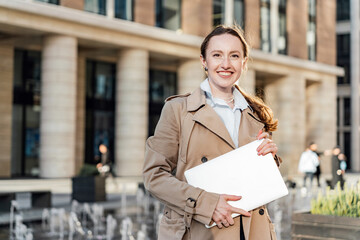 A female director holding a laptop goes to work in the office, in formal street modern clothes. ...