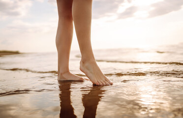 Woman leg close up walking on sand relaxing in beach at sunset. Sexy lean and tanned legs. Summer holidays.