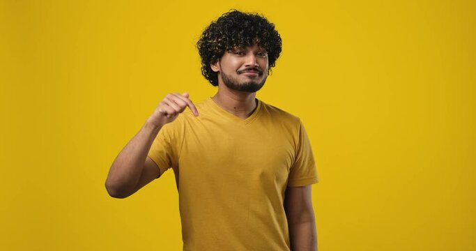 young indian man 20s wear t-shirt point index fingers down on something gesture isolated on orange studio background