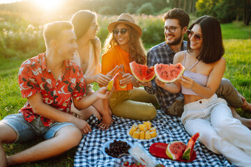 Attractive cheerful people gathering meeting eating watermelon embracing free time on the picnic  outdoors. People, lifestyle, travel, nature and vacations concept.