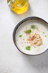 Bowl of cauliflower cream-soup on a light-beige stone background, vertical shot, high angle view