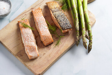 Three grilled fish steaks - red salmon with skin and green asparagus on wooden board, dill, olive oil, avocado on pastel blue background