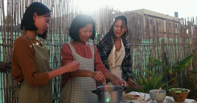 Asian family preparing together traditional thai soup at house backyard - Thai mother and adult daughters cooking together at outside kitchen