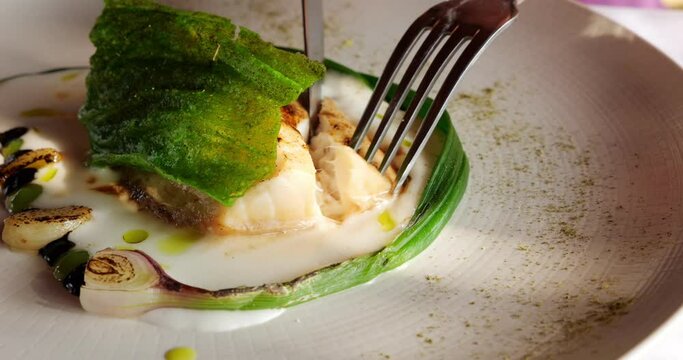In an elegant fine dining setting, close-up view captures cutting perfectly grilled sablefish steak. With skilled hand and table knife, first piece is delicately sliced from tender white flesh