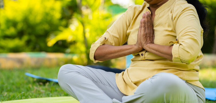 Close up shot of indian senior woman doing namaste or mudra yoga or meditation at park - concept of wellness, Active healthy lifestyle and Zen