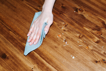 Close-up caucasian female hand wiping wooden table with rag, top view cleaning crumbs in kitchen