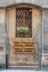 A frontal photo of a facade with and arch and a window with a shelf with flower 