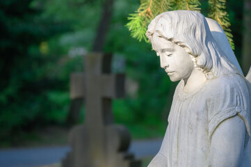 Trauernde Frauenstatue am Grabmal mit Steinkreuz im Hintergrund