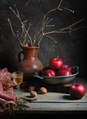 Still life with apples, tree branches in an old earthenware jug and a drink. Dark and moody - 611655451