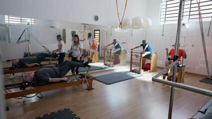Group of elderly people exercising in Pilates Studio. old age workout routine. Female coach orienting seniors to strengthen and stretch body