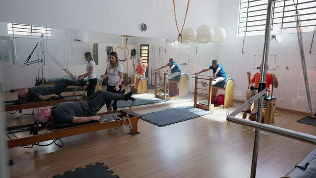 Group of elderly people exercising in Pilates Studio. old age workout routine. Female coach orienting seniors to strengthen and stretch body