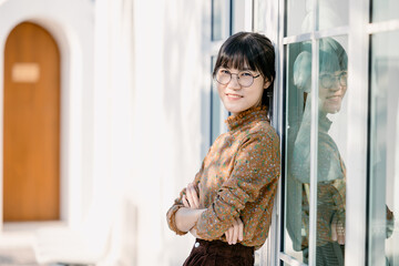 Portrait young thin glasses smiling woman looking camera crossed arms. Happy girl standing in office background. Successful Asian businesswoman standing in office.