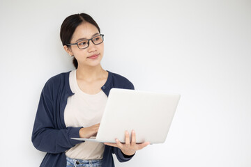 Asian teen girl with laptop computer standing on white wall thinking expression.