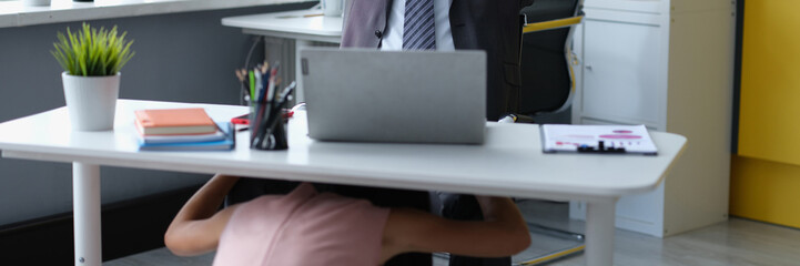Satisfied male boss at desktop and woman molest under table. Workplace harassment concept