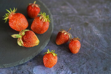 red strawberries plucked from the garden on a slate plate on a dark background close-up. The concept of nutrition with eco-friendly products from your own garden plot