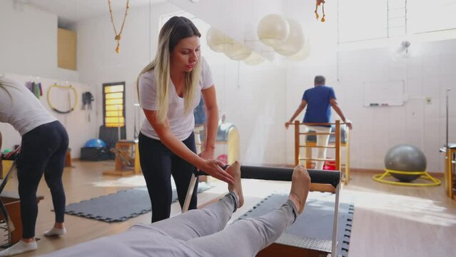 Older woman exercising in Pilates Studio Session. An elderly caucasian person laid on Machine stretching body with the guidance of Coach instructing exercise