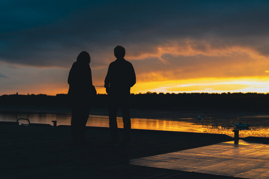 Les silhouettes d'un couple, un homme et une femme devant un couché de soleil devant la mer et une colline.