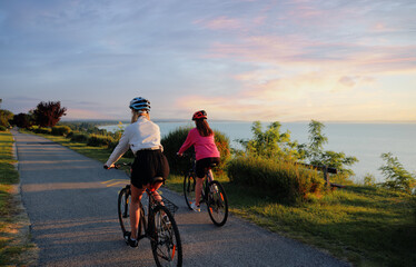 Fototapeta na wymiar Two women riding on bicycle on the sea promenade. Back view.