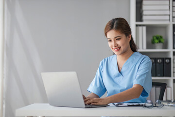 Asian doctor young beautiful woman smiling using working with a laptop computer and her writing something on paperwork or clipboard white paper at hospital desk office, Healthcare medical concept