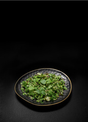 Heap of green leaves of spearmint herb on black leather background. Fresh mint leaves in a plate, top view. Template for culinary banner or flyer in dark colours for stylish food design.