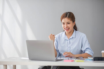 Asian businesswomen show joyful expression of success at work smiling happily with a laptop computer in a modern office.