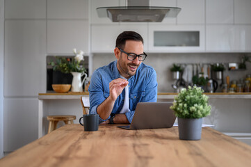 Happy businessman gesturing and discussing over video call over laptop on desk at home office