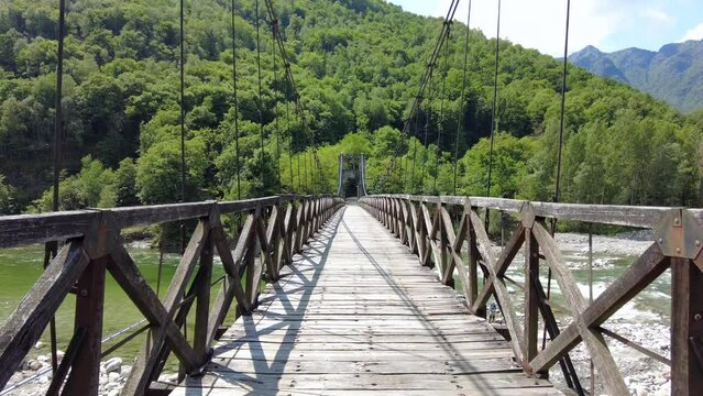 Drone flight over a wooden Tibetan suspended bridge that joins the river banks - view from the drone in Alagna Val Sesia Piedmont Alps mountains - travel concept journey in adventure natural trip 