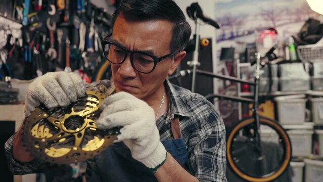 Professional senior man tightening the screw gear of bike in cycle store. Senior repairman fixing cog of bike wheel on table in bicycle shop. Maintenance and repair concept
