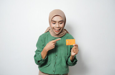Smiling young Asian Muslim woman dressed in green shirt holding credit card, online shopping isolated over white background