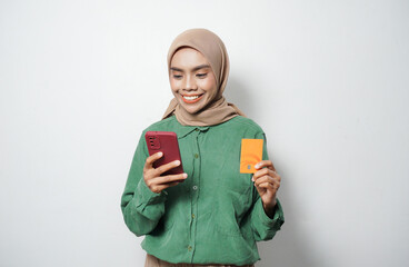 Smiling young Asian Muslim woman dressed in green shirt holding mobile phone and credit card, online shopping isolated over white background