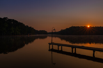 Fototapeta premium Sunrise lake light pole sunburst early morning with reflection in water of trees
